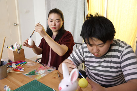 The East Asian single mother and her son are painting eggs for the upcoming Easter.
