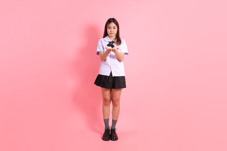 A Thai teenage girl in a school uniform standing against a pink background.の写真素材