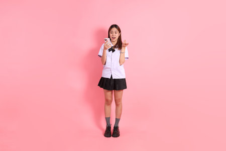 A Thai teenage girl in a school uniform standing against a pink background.の写真素材