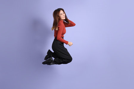 The young Southeast Asian woman in casual clothes, jumping against a purple background.の写真素材
