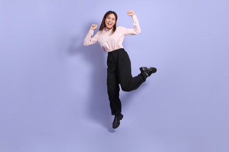 A young Southeast Asian woman in business clothes, jumping against a purple background.の写真素材