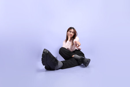 A young Southeast Asian woman in business clothes, sitting on the floor against a purple background.