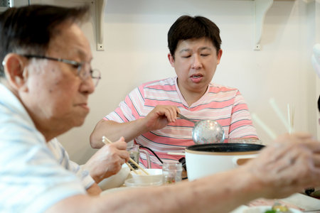 An adult East Asian man is eating sukiyaki at home with his family.の写真素材