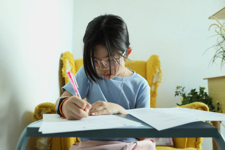 The East Asian girl is doing homework at home on the armchair.の写真素材