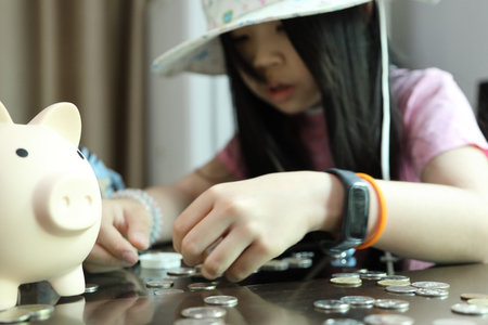An East Asian girl is counting money from her piggy bank alone in the dining room.