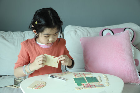 An East Asian girl assembling a wooden model house as a hobby in the living room.