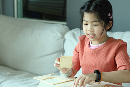 An East Asian girl assembling a wooden model house as a hobby in the living room.