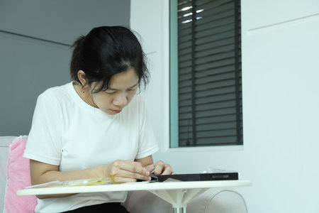 An East Asian woman checking the mail package for a smartphone screen protector and applying it to...