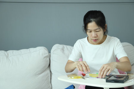 An East Asian woman checking the mail package for a smartphone screen protector and applying it to...