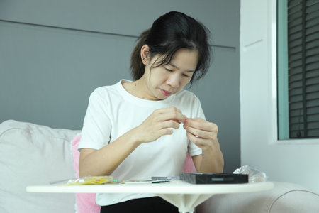 An East Asian woman checking the mail package for a smartphone screen protector and applying it to...