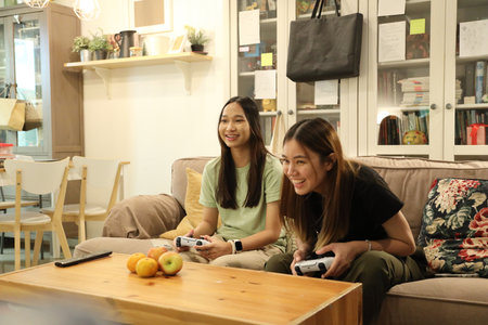 Two Southeast Asian teenage girls are playing a game together on the television.