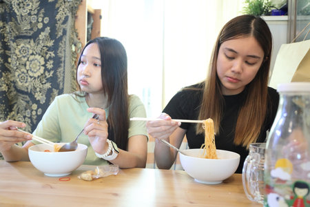 Two Southeast Asian teenage girls are eating Chinese noodles together at home.