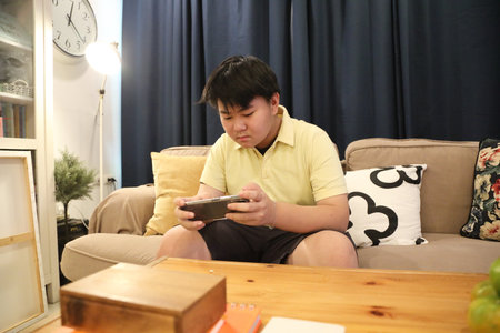 The Southeast Asian teenage boy is playing a game on his smartphone.