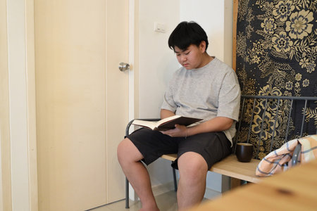 The teenager is reading a book in the house.