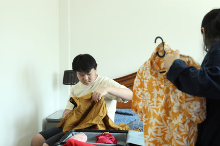 The Southeast Asian single mother is helping her teenage son pack clothes into the luggage.の写真素材