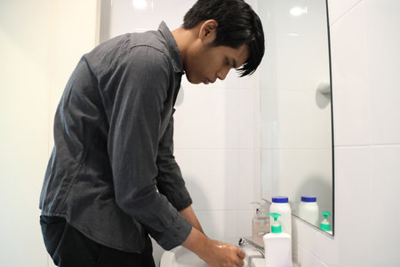 The Southeast Asian man is washing his face and styling his hair in the bathroom.