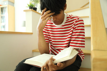 The Southeast Asian man is reading a book on the stairs.