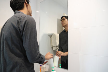 The Southeast Asian man is washing his face and styling his hair in the bathroom.