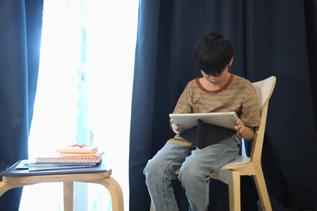 The Southeast Asian boy is using a digital tablet in the living room.