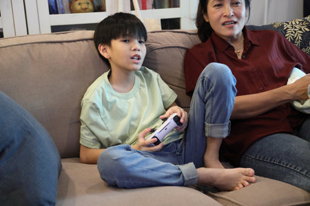 The Southeast Asian single mother is watching her teenage son play a game on the television.