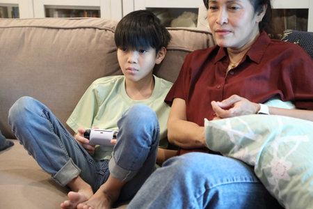 The Southeast Asian single mother is watching her teenage son play a game on the television.の写真素材