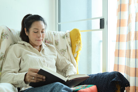 The Southeast Asian woman is reading a book in the living room.の写真素材