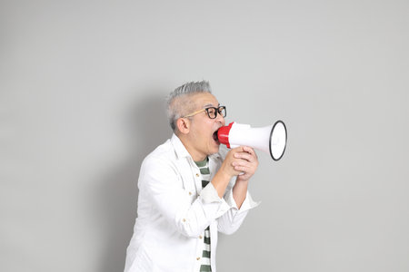 The portrait of an East Asian man with gray hair and glasses, dressed in smart casual clothes, standing against a gray background.の写真素材