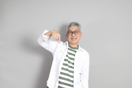 The portrait of an East Asian man with gray hair and glasses, dressed in smart casual clothes, standing against a gray background.の写真素材