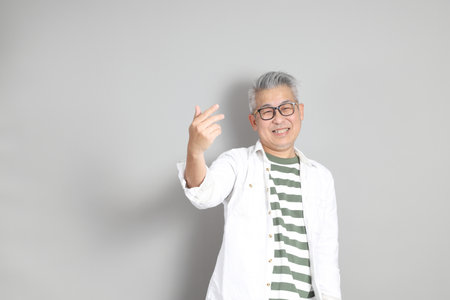The portrait of an East Asian man with gray hair and glasses, dressed in smart casual clothes, standing against a gray background.の写真素材