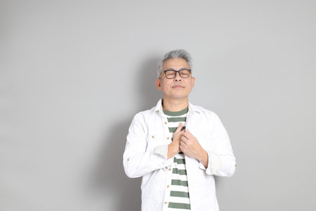 The portrait of an East Asian man with gray hair and glasses, dressed in smart casual clothes,...