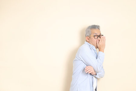 The portrait of an East Asian man with gray hair and glasses, dressed in smart casual clothes,...
