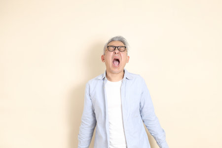 The portrait of an East Asian man with gray hair and glasses, dressed in smart casual clothes, standing against a brown background.の写真素材
