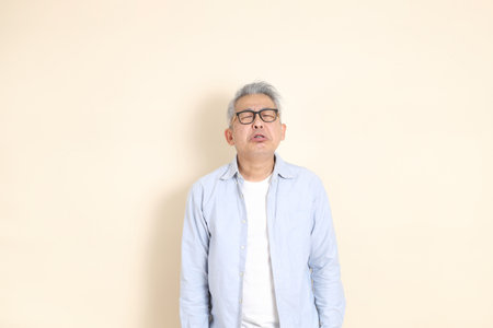 The portrait of an East Asian man with gray hair and glasses, dressed in smart casual clothes,...