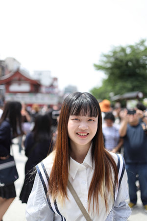The portrait shows an East Asian woman smiling at the camera while standing on a street in Asakusa,...