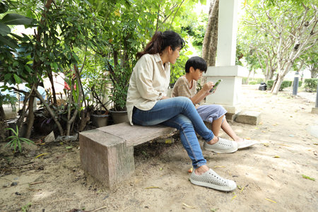 A Southeast Asian single mother spends time with her child in the park, engaging in nature-based learning activities, such as teaching about plants, insects, and the natural environment.の写真素材