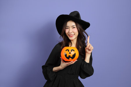 The beautiful East Asian woman in a Halloween costume is standing against a violet background.