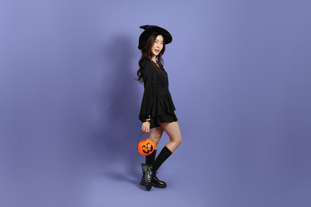 The beautiful East Asian woman in a Halloween costume is standing against a violet background.
