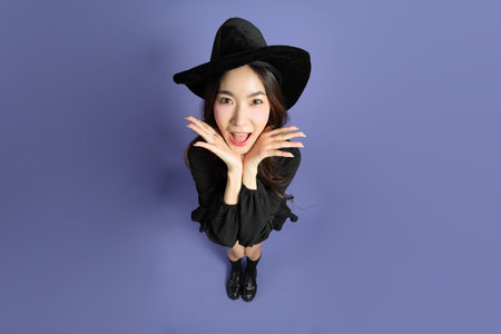 The East Asian woman in a Halloween costume is standing against a violet background.