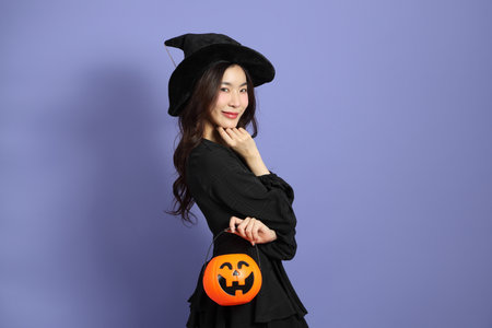 The beautiful East Asian woman in a Halloween costume is standing against a violet background.