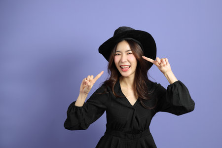 The East Asian woman in a Halloween costume is standing against a violet background.