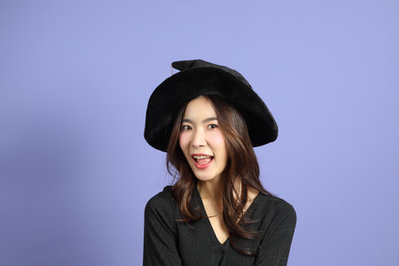 The beautiful East Asian woman in a Halloween costume is standing against a violet background.