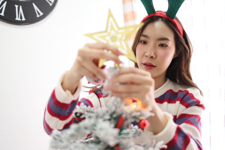 The beautiful East Asian woman is decorating the Christmas tree with a variety of ornaments for the upcoming holiday season at homeの写真素材