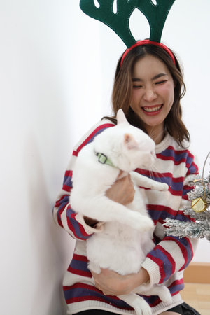 The woman is holding a cat beside the Christmas tree on a seasonal day.の写真素材