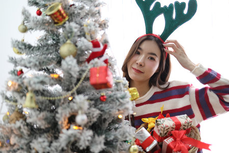The beautiful East Asian woman is decorating the Christmas tree with a variety of ornaments for the...