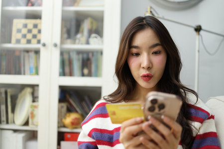 The East Asian woman is using a smartphone to do financial tasks or shop online with a credit card...