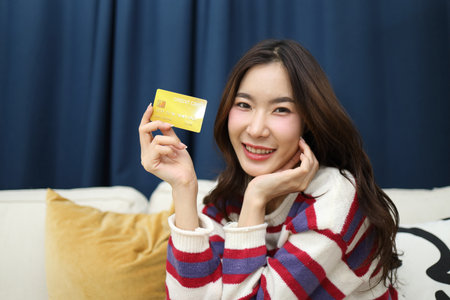 The beautiful East Asian woman is holding a credit card in the living room.の写真素材