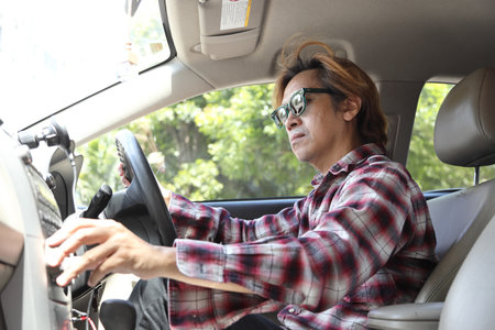 The Southeast Asian man is driving his car during the daytime.