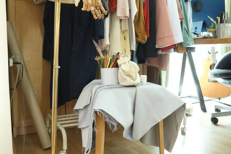 Tote bag with colored pencils and stationery placed on fabric over a stool in a clothing studio.
