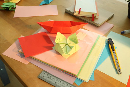 Origami lotus and boat with craft paper, steel ruler, and cutter on a workspace.