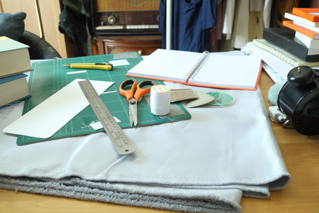 Fashion design workspace featuring sewing tools, fabric, scissors, and a cutting mat on a wooden...